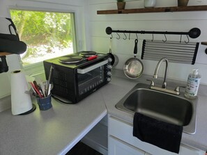 A compact kitchen with a stove, sink, and window overlooking greenery. - Rare Find: Unique Stonington Tiny House on Private Horse Farm & Kennel (Stonington)