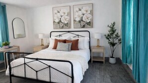 A bedroom with a bed, two bedside tables, a mirror, and a potted plant. - Sunny Poolside Retreat | Near Beach & Dining (Clearwater)