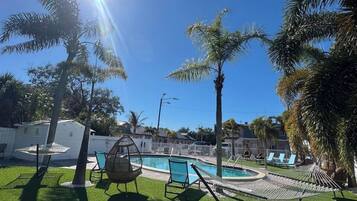 Area piscina con palme, un'amaca e una sedia a dondolo.