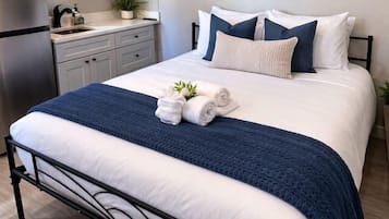 Una camera da letto con un letto, armadietti bianchi, un angolo cottura e un quadro appeso al muro.