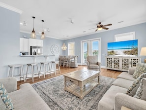 A modern living room with a coffee table, sofas, a TV, and a kitchen area with bar stools. - La Valencia Beach House (Panama City Beach)