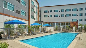 A rectangular swimming pool with lounge chairs and umbrellas, surrounded by a building with multiple windows and a flat roof. - Element by Marriott San Diego Chula Vista (Chula Vista)