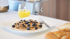 A breakfast plate with pancakes, blueberries, and granola, a glass of orange juice, and a fork on a white table. - Element by Marriott San Diego Chula Vista (Chula Vista)
