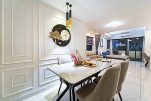 A modern living room with a dining table, sofas, and a large wall clock. - 1BR + Street-Facing Balcony - Heart of D1 (Thành phố Hồ Chí Minh)