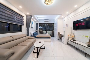 A modern living room with a sofa, a coffee table, a TV, and a wall-mounted shelf. - 1BR + Street-Facing Balcony - Heart of D1 (Thành phố Hồ Chí Minh)