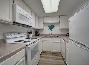 A kitchen with white cabinets, a stove, a sink, and a refrigerator. - Relax at Coral Cay #214, a spacious 2BR condo in Port Aransas, near the beach. (Port Aransas)