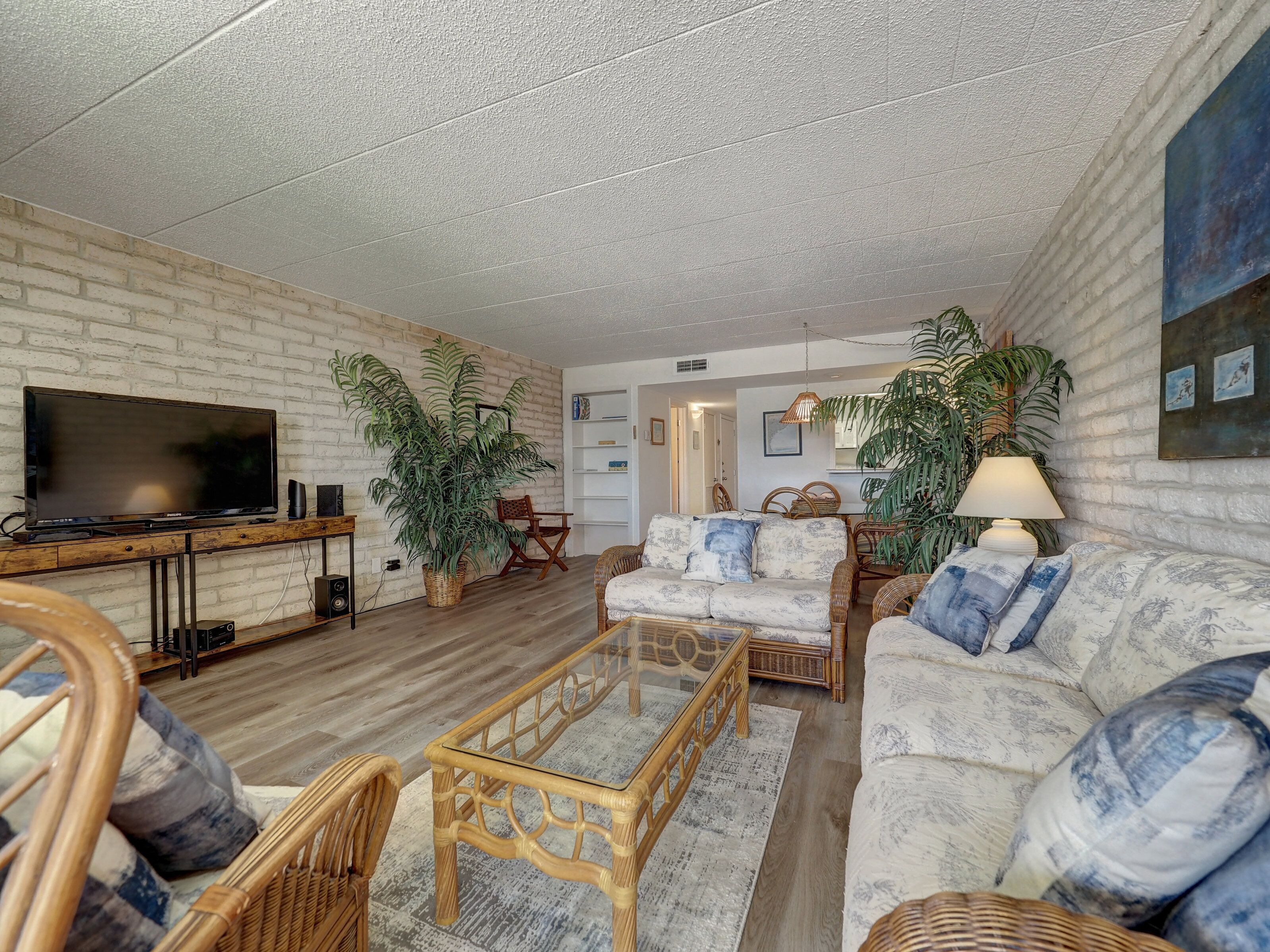 A living room with a flat-screen TV, wicker furniture, a coffee table, and potted plants.
