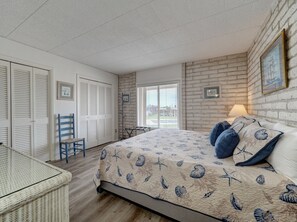 A bedroom with a bed, a chair, a table, and a window with blinds. - Relax at Coral Cay #214, a spacious 2BR condo in Port Aransas, near the beach. (Port Aransas)
