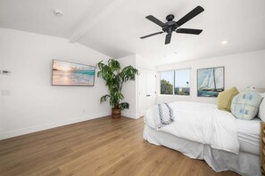 Ein Schlafzimmer mit einem Bett, einem Deckenventilator, einem großen Fenster und einer Topfpflanze.