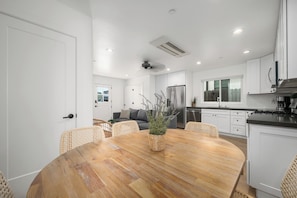 Eine moderne Küche mit weißen Schränken, einem Edelstahlkühlschrank und einem Essbereich mit Holztisch und Korbstühlen.