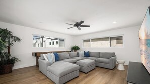 A modern living room with a sectional sofa, a ceiling fan, and large windows. - Large Newport Beach Home Walk to the Beach (Newport Beach)