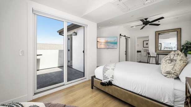 A bedroom with a bed, a ceiling fan, a sliding glass door leading to a balcony, and a painting on the wall. - Large Newport Beach Home Walk to the Beach (Newport Beach)