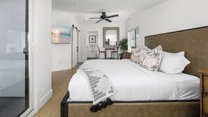 A modern bedroom with a large bed, a ceiling fan, a TV, and a view of the room through a sliding door. - Large Newport Beach Home Walk to the Beach (Newport Beach)