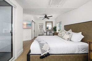 A modern bedroom with a large bed, a ceiling fan, a TV, and a view of the room through a sliding door. - Large Newport Beach Home Walk to the Beach (Newport Beach)