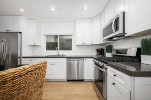A modern kitchen with white cabinets, stainless steel appliances, and a wooden floor. - Large Newport Beach Home Walk to the Beach (Newport Beach)
