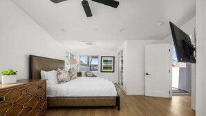A bedroom with a bed, a nightstand, a lamp, a plant, and a TV. - Large Beachside Escape in Prime Location (Newport Beach)