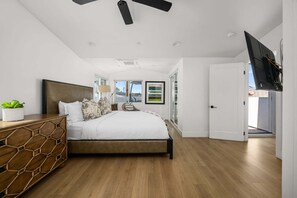 Ein Schlafzimmer mit einem Bett, einem Nachttisch, einer Lampe, einer Pflanze und einem Fernseher.