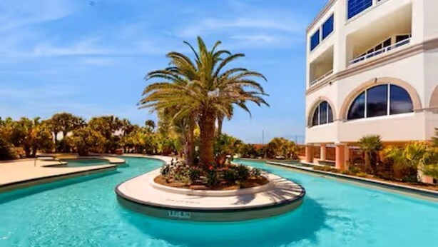 A hotel with a pool, palm trees, and a two-story building with arched windows. - Emerald Suite 607 ~ Luxury 3BR Oceanfront + Full Resort Amenities Included (Galveston)