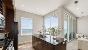 A modern kitchen with a large island, a view of the ocean, and a balcony with a view. - Emerald Suite 607 ~ Luxury 3BR Oceanfront + Full Resort Amenities Included (Galveston)