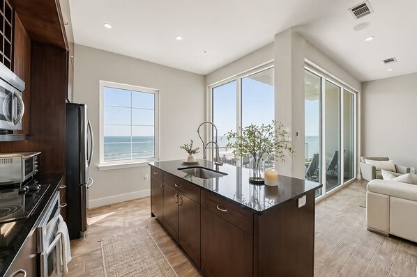 A modern kitchen with a large island, a view of the ocean, and a balcony with a view. - Emerald Suite 607 ~ Luxury 3BR Oceanfront + Full Resort Amenities Included (Galveston)