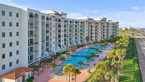 A multi-story hotel with a central pool area, outdoor seating, and palm trees. - Emerald Suite 607 ~ Luxury 3BR Oceanfront + Full Resort Amenities Included (Galveston)