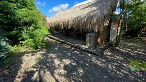 A rustic thatched-roof structure with a wooden bench and a small table, surrounded by dense greenery. - KAY TI CANNELLE (Le Diamant)