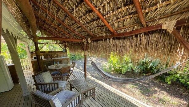 A wooden deck with a thatched roof, a hammock, and a seating area with cushions. - KAY TI CANNELLE (Le Diamant)