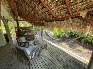 A wooden deck with a thatched roof, a hammock, and a seating area with cushions.