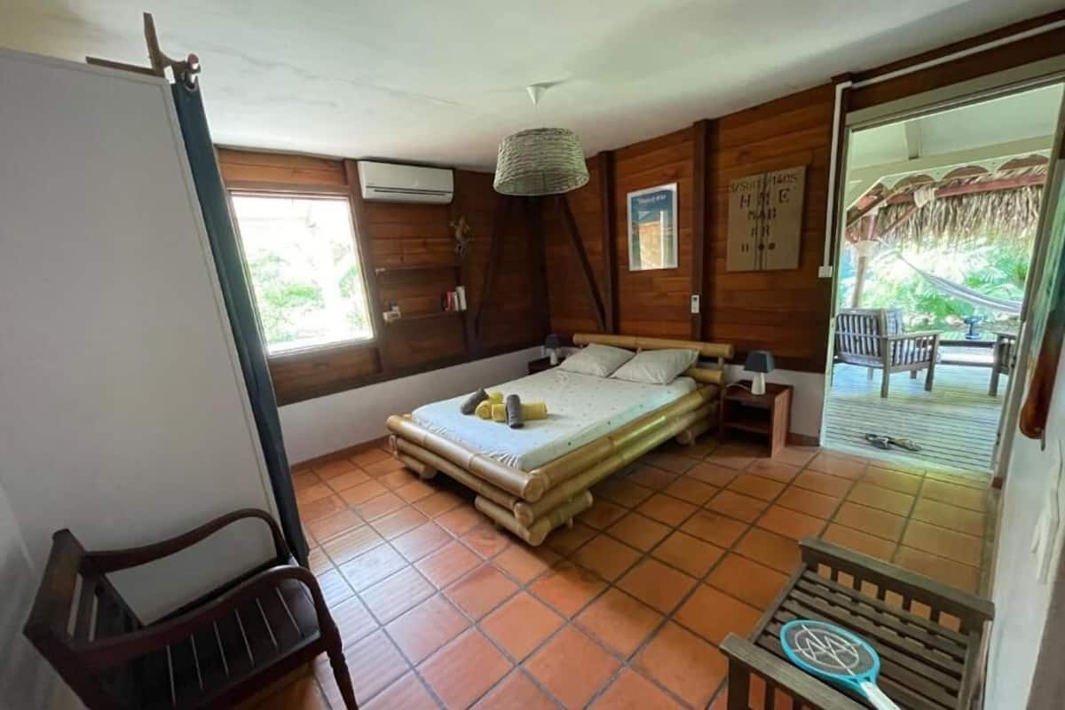 A room with a bed, a chair, a table, and a view of the outside.