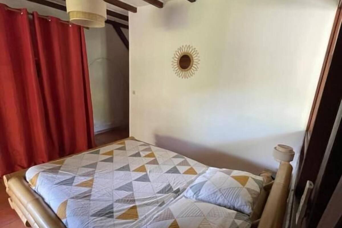 A bed with a geometric-patterned bedspread, a wooden headboard, a red curtain, and a ceiling with exposed beams.