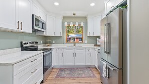 Une cuisine moderne avec des meubles blancs, des appareils en acier inoxydable, une grande fenêtre et un tapis à motifs.