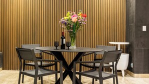 Een vergaderruimte met een ronde tafel, vier stoelen, een vaas met bloemen en een fles wijn.