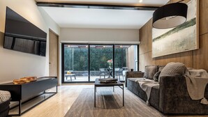 Een moderne woonkamer met een bank, een salontafel, een aan de muur bevestigde televisie en een groot raam met uitzicht op het omliggende landschap.