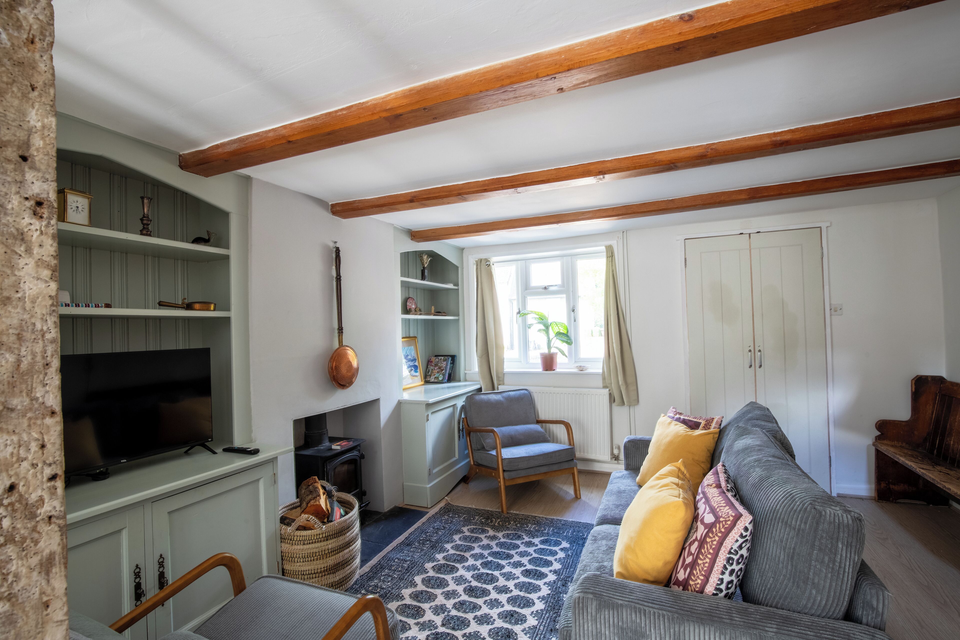 A living room with a television, wooden beams, a sofa, and a window with curtains.