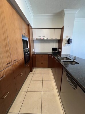 A modern kitchen with wooden cabinets, a built-in oven, a microwave, a sink, and a phone on the wall. - `Beside Still Waters` Luxury Escape (Surfers Paradise)