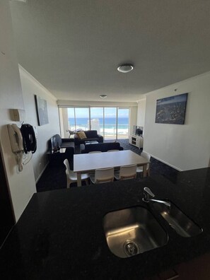 A modern hotel room with a dining area, a kitchenette, and a large window offering a view of the beach. - `Beside Still Waters` Luxury Escape (Surfers Paradise)