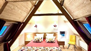 Quarto no sótão com cama, vigas de madeira, uma janela e um abajur.