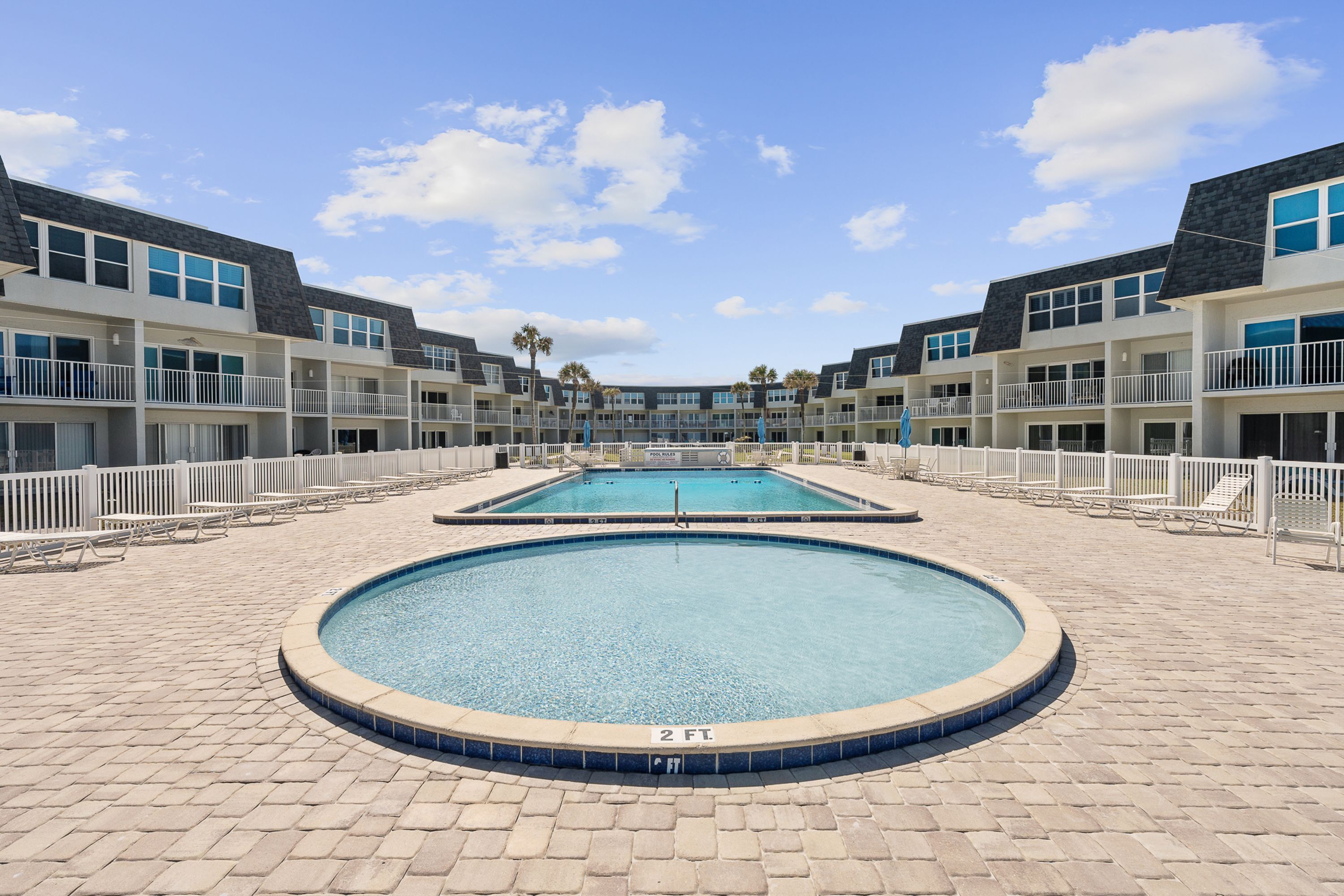 Ein Poolbereich mit zwei Pools, weißen Geländern und blauem Himmel.