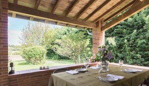 An outdoor dining area with a brick wall, wooden ceiling, and a view of a garden. - La Mansou - VALLESVILLES (VALLESVILLES)