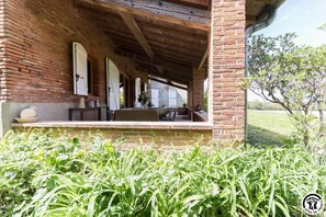 Un edificio de ladrillo con un porche cubierto, una mesa con sillas y un jardín al frente.