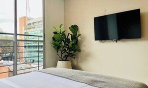 Ein Hotelzimmer mit Bett, Zimmerpflanze, Flachbildfernseher und großem Fenster mit Blick auf die Stadt.