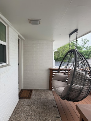 A hanging chair with cushions, a wooden bench, a white brick wall, and a door.