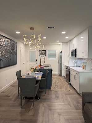 A modern kitchen with white cabinets, a central island, and a dining area with wicker chairs.