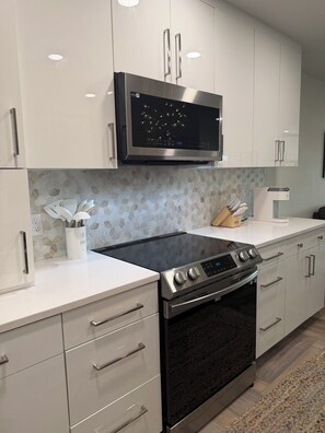 A modern kitchen with white cabinets, a stainless steel microwave, a black stove, and a tiled backsplash.