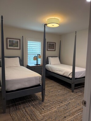 A bedroom with two four-poster beds, a patterned rug, and framed artwork on the walls.