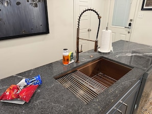 A kitchen with a stainless steel sink, a faucet, a paper towel holder, and a bottle of hand soap.
