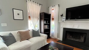Een woonkamer met een witte bank, een zwarte salontafel met een plant, een open haard en een boekenkast.