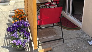 Un patio con un separador de madera, una mesa con sillas rojas y un ventanal corredero que da a un dormitorio.
