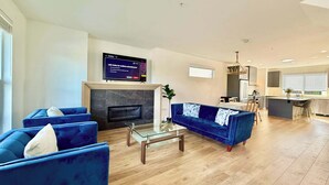A modern living room with a fireplace, blue sofas, a coffee table, and a TV mounted on the wall. - Luxury 3Br, Oasis Gated, Yard Pets Welcome (Langley Township)