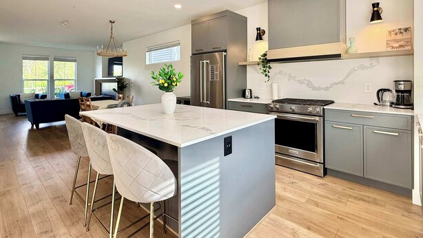 A modern kitchen with a central island, stainless steel appliances, and a dining area with a sofa and chairs. - Luxury 3Br, Oasis Gated, Yard Pets Welcome (Langley Township)